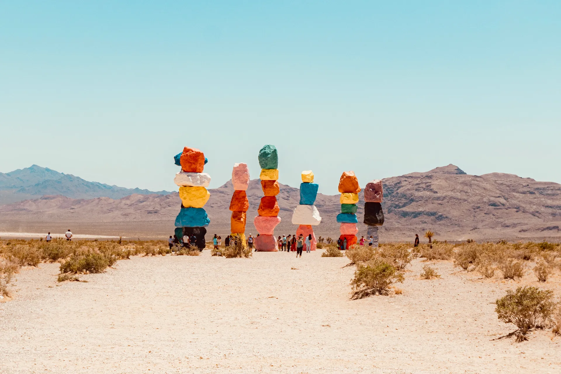 Torres de rocas apiladas y pintadas de colores llamativos en pleno desierto de Nevada, con montañas áridas al fondo y visitantes a sus pies